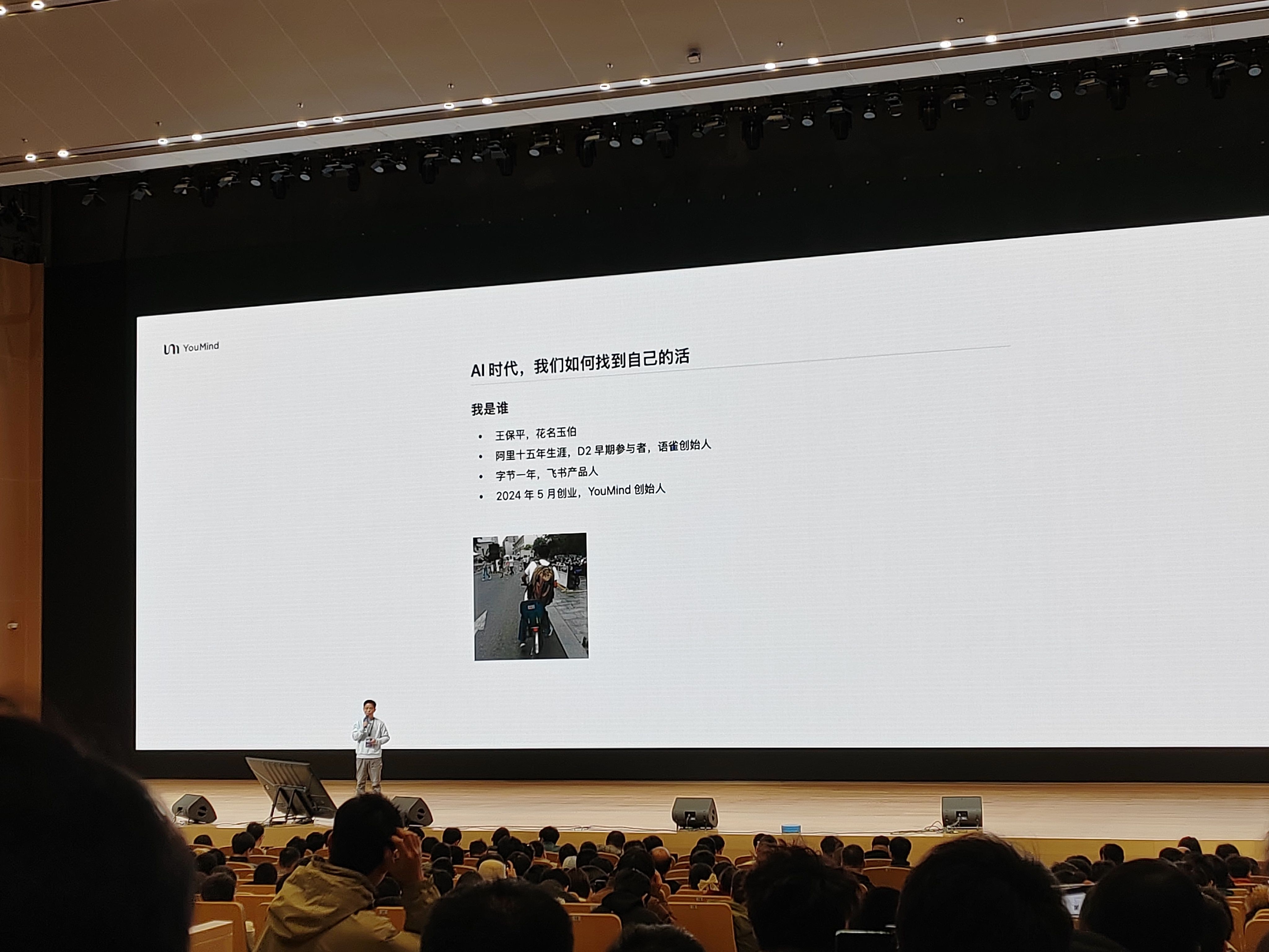 演讲者介绍 “AI 时代,我们如何找到自己的活”,背景屏显示个人信息 —— 花名玉伯,阿里十五年资深成员、语雀创始人等身份,屏幕下方有一张人物照片,演讲者站在舞台中央,与台下观众互动。