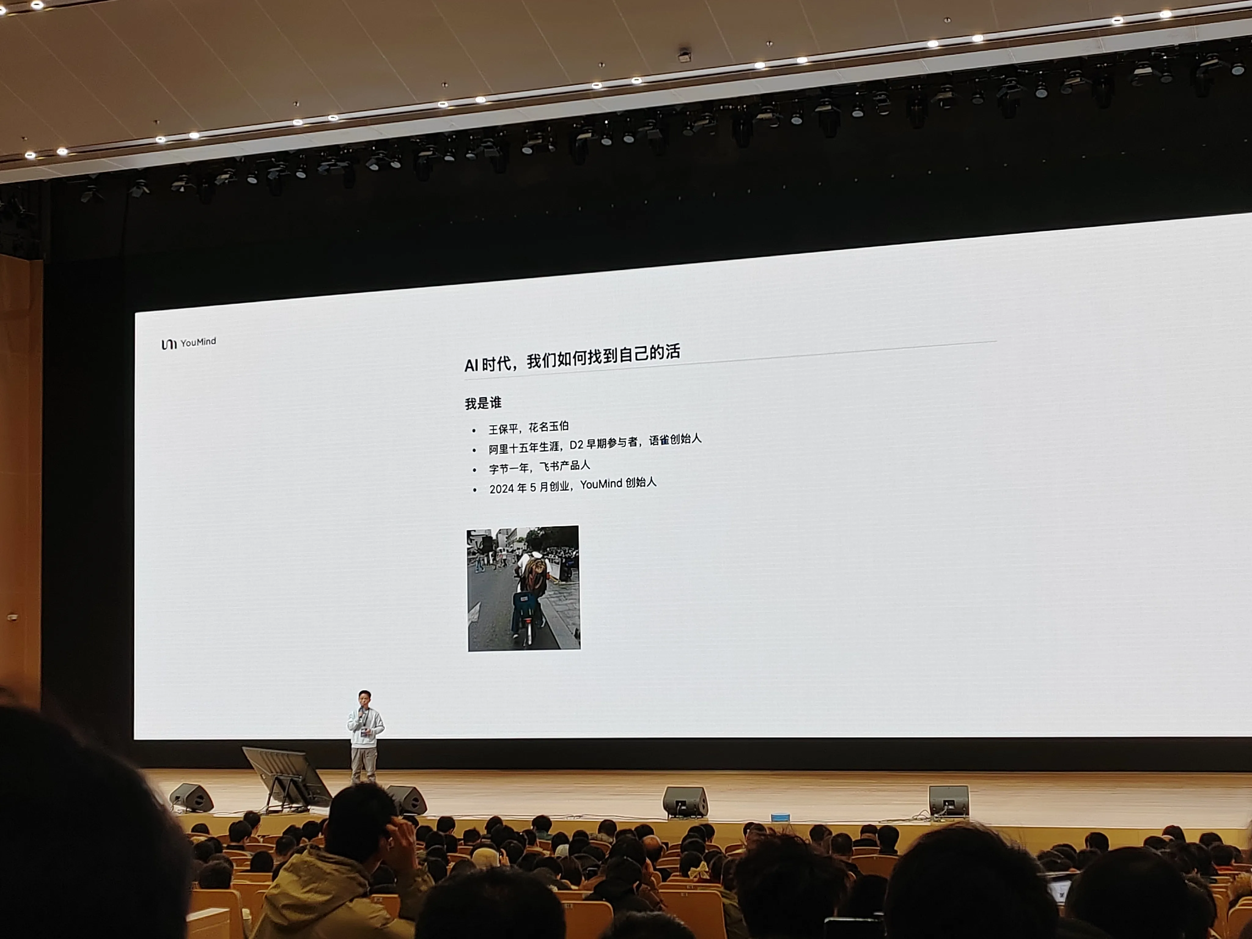 演讲者介绍 “AI 时代，我们如何找到自己的活”，背景屏显示个人信息 —— 花名玉伯，阿里十五年资深成员、语雀创始人等身份，屏幕下方有一张人物照片，演讲者站在舞台中央，与台下观众互动。