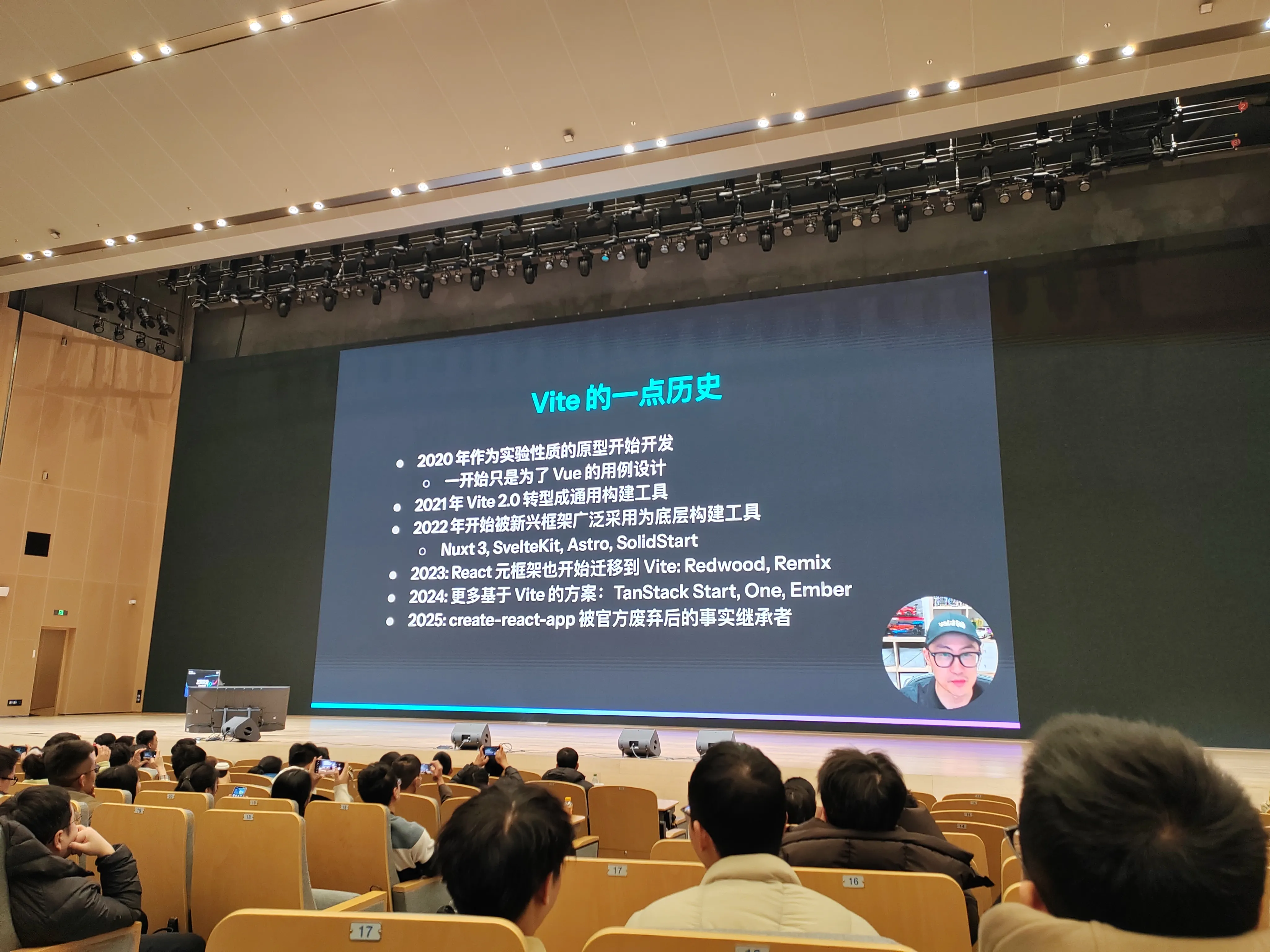 vuejs作者尤雨溪聊前端工具链,背景屏展示 “Vite 的一点历史”，罗列 2020 至 2025 年关键发展节点（如 2020 年实验性开发、2021 年 Vite 2.0 转型等），台下观众面向舞台，聚焦 Vite 技术演进内容。