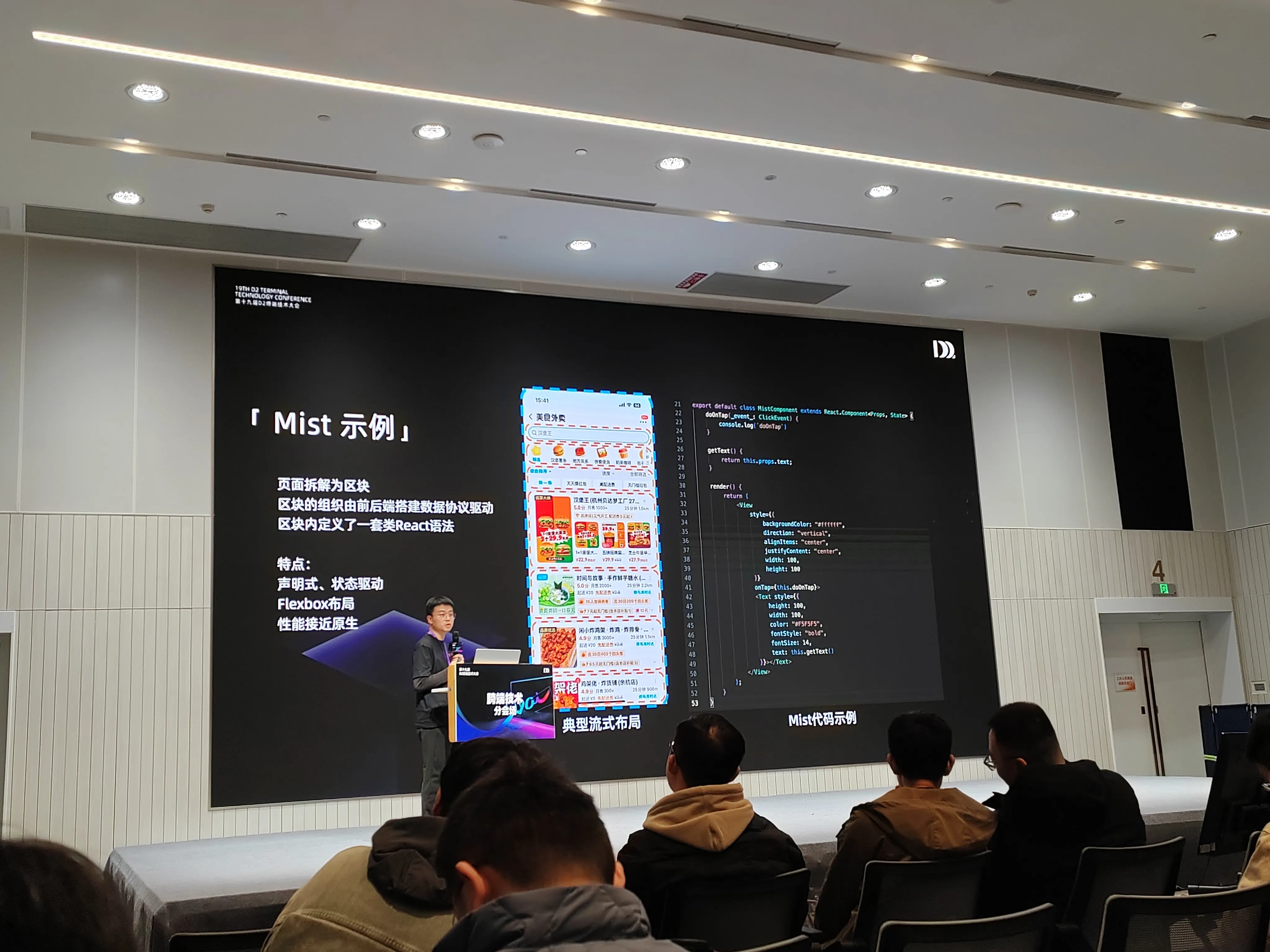 会议分会场中,演讲者站在讲台后介绍 “Mist 示例”,背景大屏左侧说明 “页面拆解为区块,由前后端搭建数据协议驱动,区块内定义类 React 语法”,并列出 “声明式、状态驱动、Flexbox 布局、性能接近原生” 等特点;中间展示外卖类应用的典型流式布局页面截图,右侧呈现 Mist 代码示例,台下参会者面向舞台专注聆听。