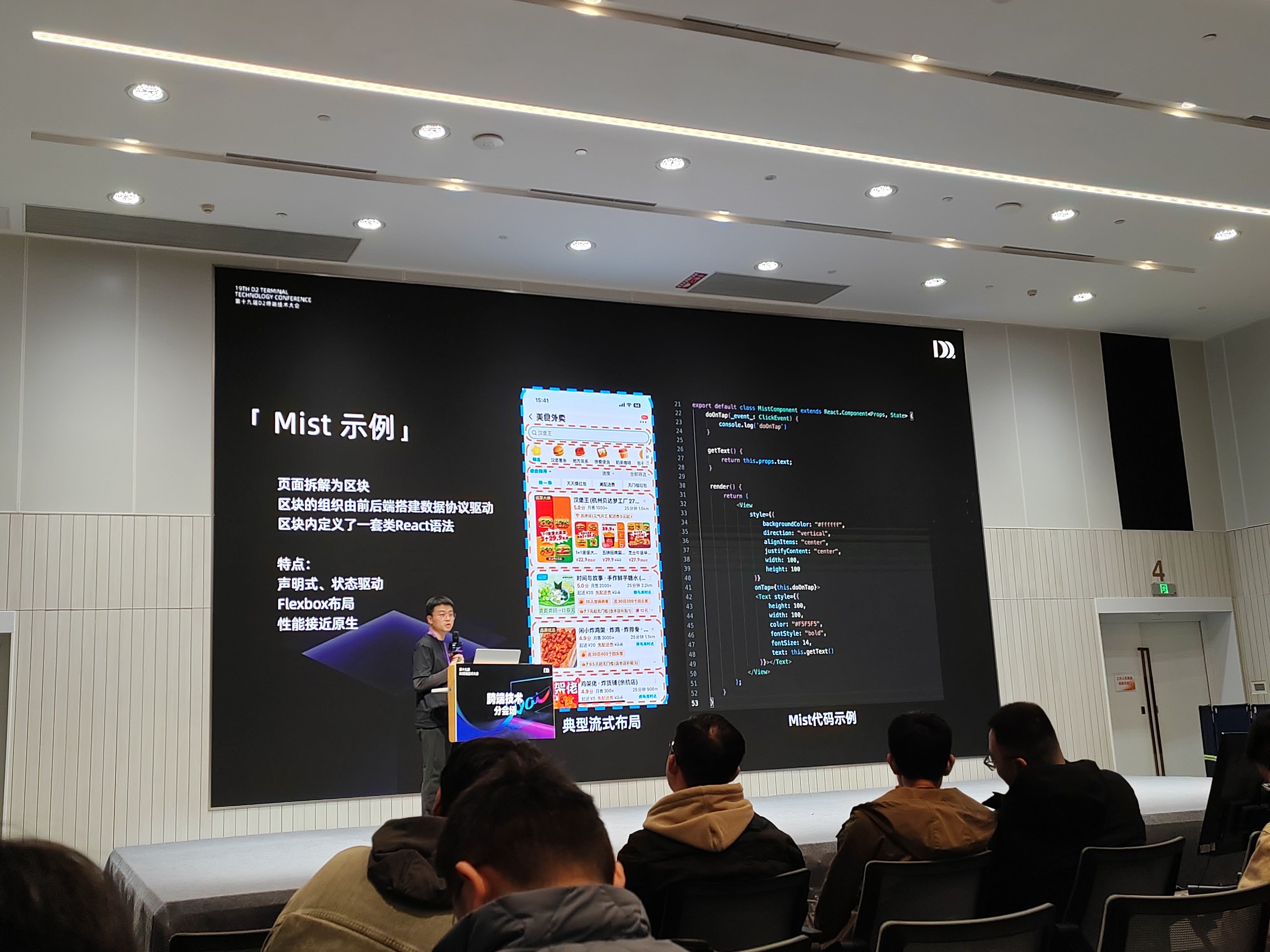 会议分会场中,演讲者站在讲台后介绍 “Mist 示例”,背景大屏左侧说明 “页面拆解为区块,由前后端搭建数据协议驱动,区块内定义类 React 语法”,并列出 “声明式、状态驱动、Flexbox 布局、性能接近原生” 等特点;中间展示外卖类应用的典型流式布局页面截图,右侧呈现 Mist 代码示例,台下参会者面向舞台专注聆听。